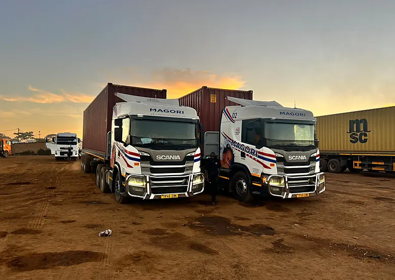 Two Magori Logistics trucks with containers at dusk