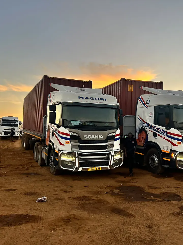 Two Magori Logistics trucks with containers at dusk
